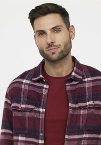 Chemise en flanelle à carreaux prune avec des rayures blanches et navy en contraste, dotée de poches poitrine boutonnées et d'un t-shirt rouge en col rond en dessous.