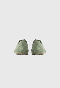 Ein Paar grüne Wildlederschuhe für die Freizeit, von hinten gezeigt, vor einem schlichten weißen Hintergrund.