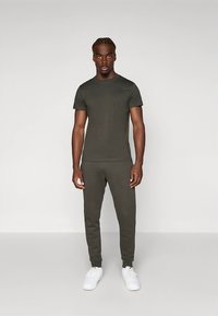 Olivno zelena oprijeta majica s kratkimi rokavi in jogger hlače iz mehke tkanine, kombinirane z belimi supergami. Preprost dizajn s kratkimi rokavi in elastičnim pasom.