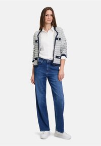 Karoblauer und weißer Cardigan mit runden Knöpfen, über einem weißen Hemd getragen. Kombiniert mit lockeren blauen Jeans und weißen Sneakers.