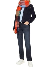 Marineblauwe corduroy jasje, lichtblauw shirt, donkere spijkerbroek, meerkleurige geblokte sjaal, witte platform sneakers. De sjaal heeft franjes.