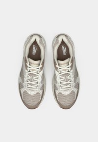 Light gray mesh running shoes with cream accents, featuring a cushioned sole, lace-up design, and logo detailing on the tongue.