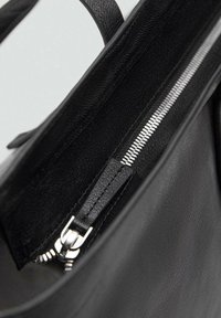 Intérieur d'un sac à main en cuir noir avec une poche zippée en métal argenté. Le matériau texturé et la doublure lisse créent un contraste.