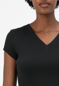 Black ribbed short-sleeve top with a V-neck design. Textured fabric, close-fitting cut, and visible stitching details along the neckline.