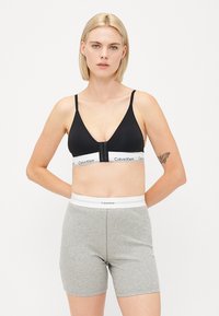 Čierny bezdrôtový bralet s hlbokým výstrihom a predným zapínaním, doplnený o šedé rebrované boxerky s bielym brandovaným pásom.