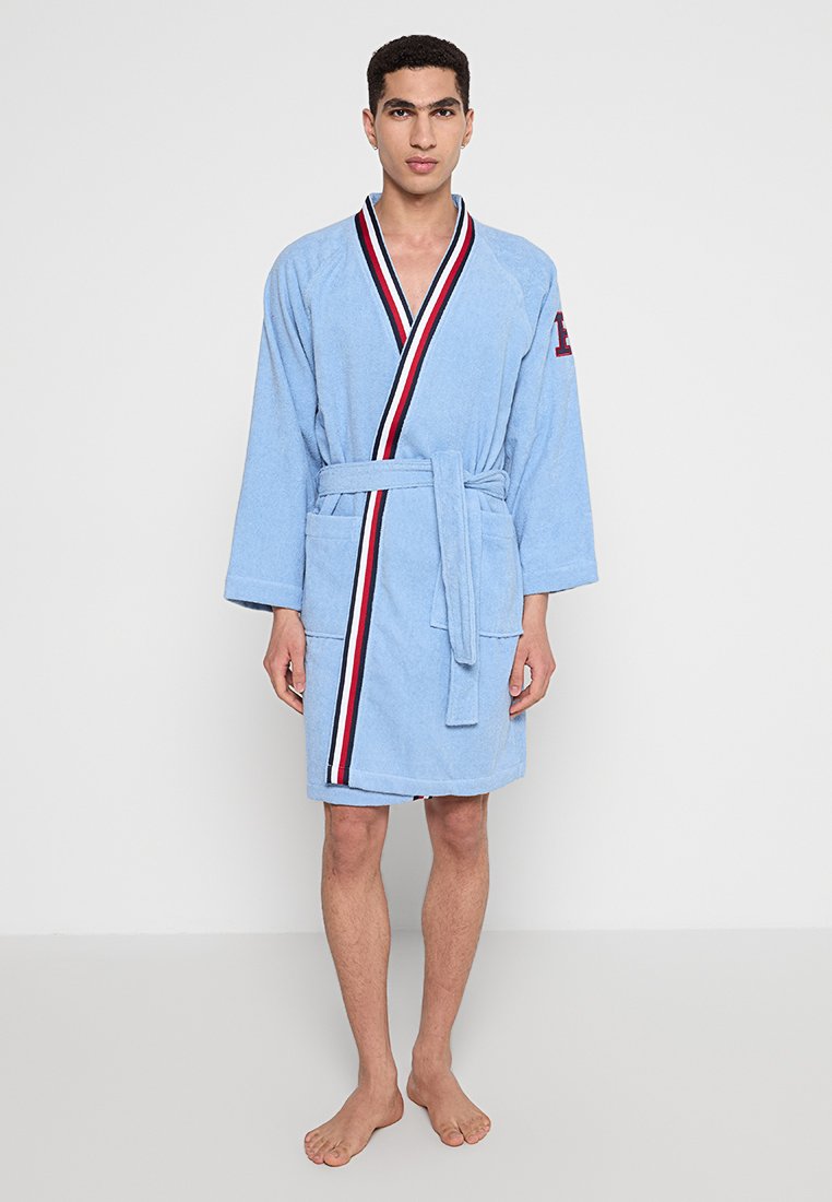 Blaues Frottee-Bademantel mit Schalkragen, Gürtel in der Taille und seitlichen Taschen. Verziert mit roten und weißen Streifen entlang der Vorderseite.