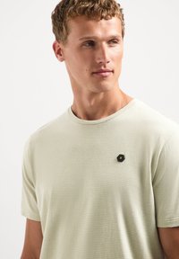 Lichtgroene gestreepte t-shirt met korte mouwen van zachte stof, met een klein zwart hexagonaal logo op de borst.