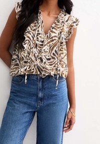 Luftig, beige blus med djurmönster, volangkrage och knytdetaljer, matchad med högmidjade blå denimjeans.