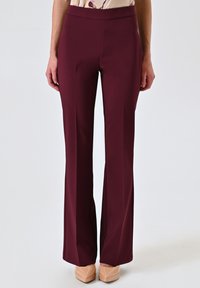Bordeaux kleurige op maat gemaakte broek met een uitlopende pijp. Gemaakt van een gladde, rekbare stof. Voorzien van een hoge tailleband voor een comfortabele pasvorm.