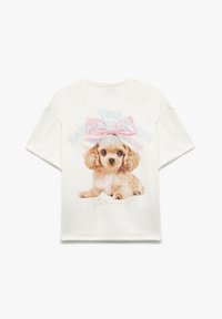 Cremefarvet t-shirt med korte ærmer, der viser en trykt illustration af en brun hvalp med en pink sløjfe og tekst, der siger "Din lykke er din superkraft."
