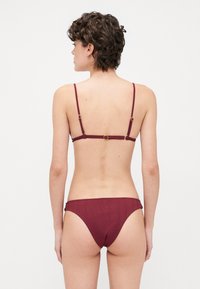 Maroon bikini set, featuring thin adjustable straps, ribbed texture, and a classic cut. Gold hardware accents on the back closure.