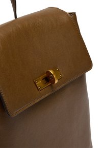 Brązowy skórzany plecak z klapą, z metalowym zapięciem w złotym odcieniu oraz subtelną fakturą. Gładkie krawędzie i detale szycia.