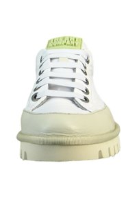 White sneaker with beige rubber sole, round toe, and green logo patch. Features white laces and silver metal eyelets.