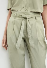 Jasnooliwkowe spodnie z paskiem w talii, z plisami, gładką teksturą i luźnym krojem. Zaprojektowane z myślą o komforcie i wszechstronności.