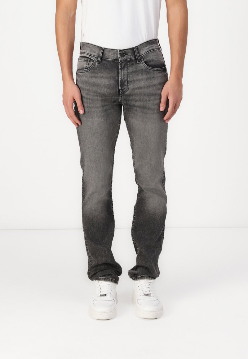 Grå denimjeans med en falmet finish, fem lommer og rett benkutt. Kombinert med hvite joggesko og en enkel hvit t-skjorte.