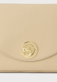 Smėlio spalvos odinis delninukas su tekstūruotu paviršiumi, puoštas apvalia aukso spalvos užsegimo sagtimi ir kontrastingomis siūlėmis kraštuose.