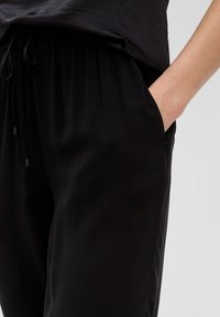 Zwarte broek met een ontspannen pasvorm, uitgerust met een elastische tailleband en trekkoord. Zijzakken hebben een gladde textuur, geschikt voor casual kleding.