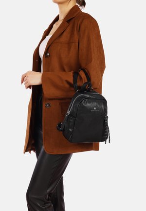 Zaino in pelle nera con finitura texturizzata, chiusura con zip e doppi manici. Ambientato su un blazer in suede marrone e pantaloni neri.