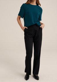 Teal kortärmad topp med en texturerad yta, kombinerad med svarta skräddarsydda byxor. Skorna består av svarta, vadderade ballerinas.