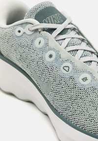 Jasnoszare trampki z teksturowanej siateczki, gumową podeszwą i dekoracyjnymi guzikami w wzór falisty. Zawierają subtelne logo Nike.