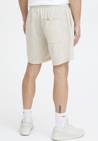 Lyse beige shorts laget av teksturert stoff, med elastisk midjebånd og en sidelomme på høyre side. God passform og kne-lengde.