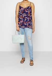 Laivansininen kukallinen ilmanhiha toppi, vaaleansiniset revenneet skinny-farkut, mustat nauhakengät, kantaa tikkauksella varustettua vaaleansinistä käsilaukkua.