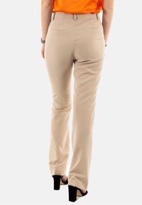 Beżowe spodnie o dopasowanym kroju, z gładką teksturą i prostymi nogawkami. Posiadają tylne kieszenie oraz średni stan. W zestawie z czarnymi szpilkami.