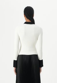 White ribbed long-sleeve top with a black collar, paired with a black pleated skirt. Features a fitted design and contrasting cuffs.