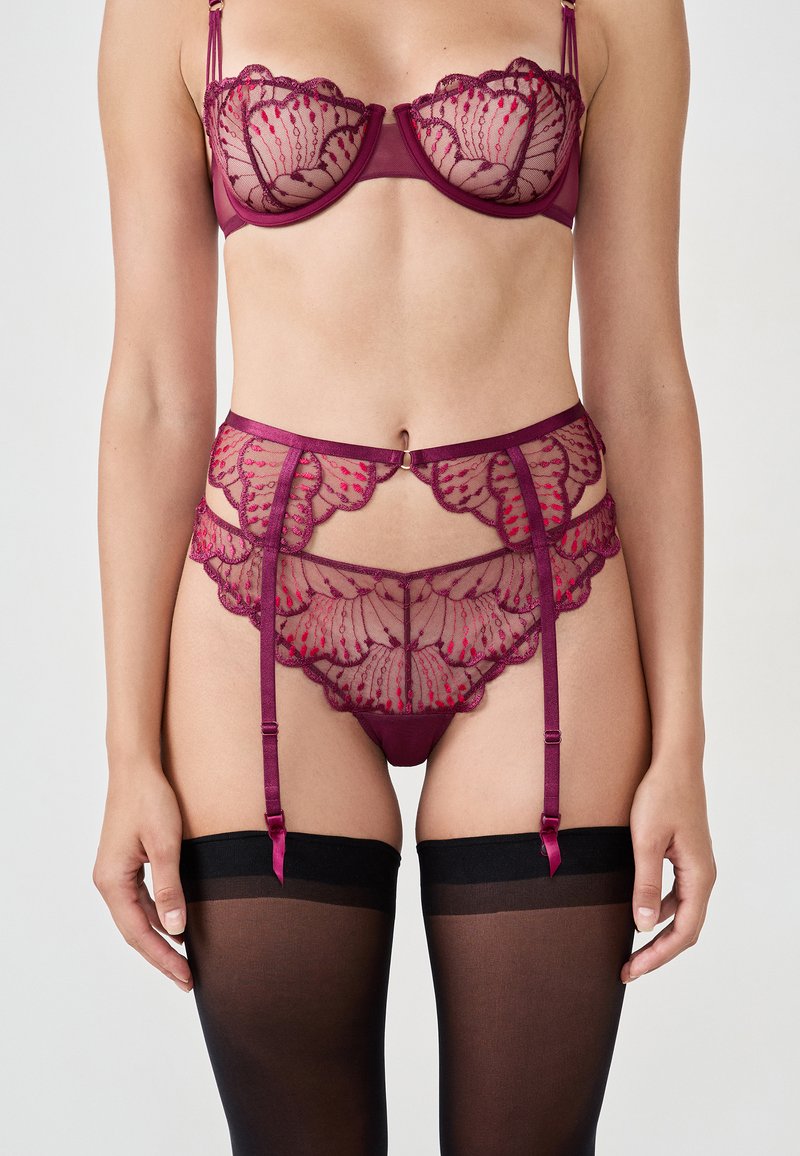 Completo di lingerie in pizzo borgogna, composto da un reggiseno semi-trasparente con motivi floreali, una cintura per reggicalze abbinata e calze nere con accenti in raso.