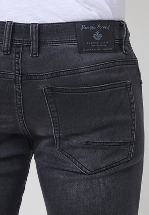 Czarne dżinsy o gładkiej fakturze, klasyczny pięciokieszeniowy fason oraz metka marki na pasku z logo liścia.