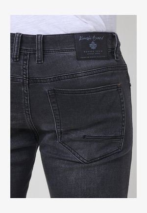 Czarne dżinsy o gładkiej fakturze, klasyczny pięciokieszeniowy fason oraz metka marki na pasku z logo liścia.