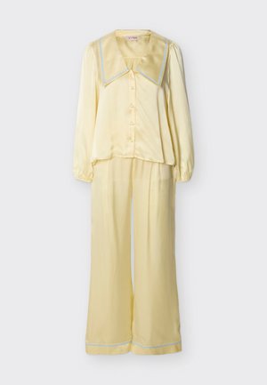Μαλακό κίτρινο σατέν μακρυμάνικο πουκάμισο με κουμπιά, φαρδύ γιακά και παντελόνι με φαρδιά μπατζάκια, και τα δύο διακοσμημένα με γαλάζιες κυματιστές άκρες.
