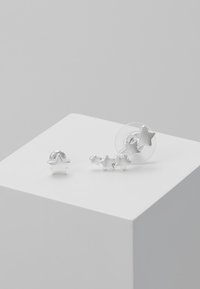 Sølv stjerneformede øreringe med en stor stud og et sæt af mindre sammenkoblede stjerner. Glat overflade med en poleret metallisk finish.