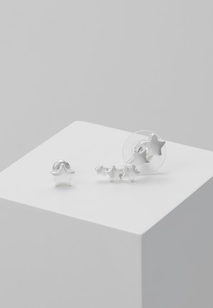 Silverskimrande stjärnformade örhängen som har en stor stud och en uppsättning mindre sammankopplade stjärnor. Slät yta med en polerad metallisk finish.