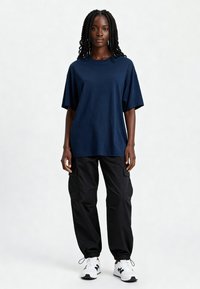 Jūras spēku oversized kokvilnas t-krekls ar īsām piedurknēm, apvienots ar melniem cargo biksēm ar elastīgām aprocēm un kabatām. Apavi ir balti ar melniem akcentiem.