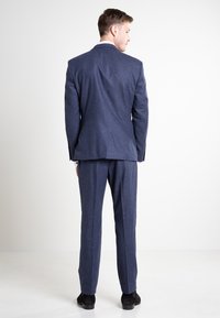 Dunkelblauer Anzug mit glatter Textur, tailliertem Schnitt, Einzelschlitz und passenden Hosen. Abgerundet mit schwarzen Schuhen.