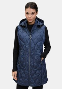 Námořnická prošívaná vesta s kapucí, předním zipem a dvojitými bočními kapsami. Obsahuje texturovaný vzor a krátký lem. Vyrobena z lehkého materiálu.