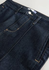 Jeans de mezclilla azul oscuro con costuras amarillas, diseño de cinco bolsillos y cierre frontal de botón. Textura suave y ajuste clásico.