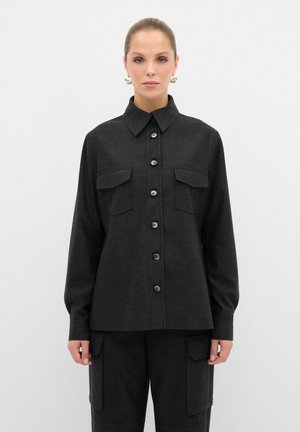 Camisa negra de botones con cuello, dos bolsillos en el pecho y mangas largas, hecha de una tela texturizada. Los botones son de color azul oscuro.