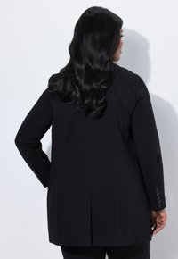 Blazer nero con una vestibilità sartoriale, caratterizzato da una fessura singola sul retro e dettagli con bottoni sulle maniche. Tessuto dalla superficie liscia.
