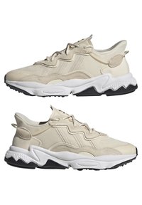 Beige sneakers featuring a textured mesh upper, three-dimensional contours, and a thick white midsole with a black rubber outsole.
