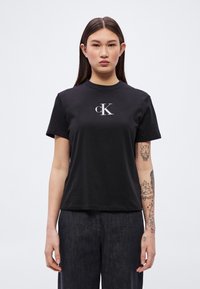 Svart bomulls-T-skjorte med korte ermer og rund hals, med en kontrasterende sølvfarget brodert cK-logo på brystet. Casual passform.