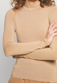 Maglione beige a maniche lunghe con collo alto, realizzato in tessuto liscio e elastico; design aderente con colletto alto e maniche sottili. Tessuto uniforme, senza fantasie.