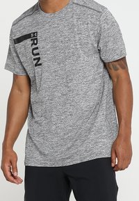 T-shirt sportivo grigio con maniche corte, realizzato in tessuto testurizzato. Presenta una stampa nera "RUN" sul davanti, inclinata attraverso il petto.