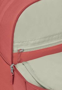 Coin de sac à dos rouge et beige; présente une fermeture éclair, un tissu texturé, et un accent de couleur contrastante le long du bord et de la zone de la fermeture éclair.