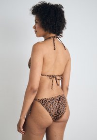 Bikini s uzorkom leopard, smeđa boja s crnim mrljama, trokutasti gornji dio s vezicama oko vrata i srednje visoki donji dio. Glatka tekstura i minimalno pokrivanje.