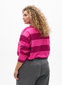 Pink striped long-sleeve shirt with a relaxed fit, featuring wide horizontal stripes in varying shades. Paired with gray pinstriped trousers.