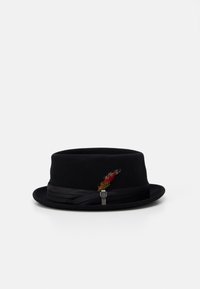 Chapeau en feutre noir avec un bord étroit, orné d'un bandeau en satin et d'une plume décorative avec des accents rouges et verts.