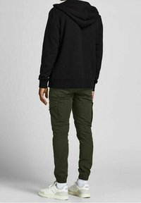 Sort hættetrøje med hætte, sat sammen med olivengrønne cargo-bukser med sidelommer. Hvide sneakers fuldender outfittet.