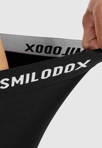 Czarne spodenki sportowe z szerokim pasem, na którym widnieje biały napis "SMILODOX". Materiał wydaje się elastyczny i gładki. Zbliżenie na pas.